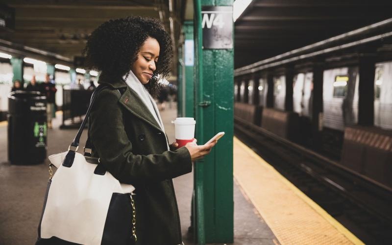 Find your perfect fit at The Katharine woman with a cup of coffee texts on subway station platform